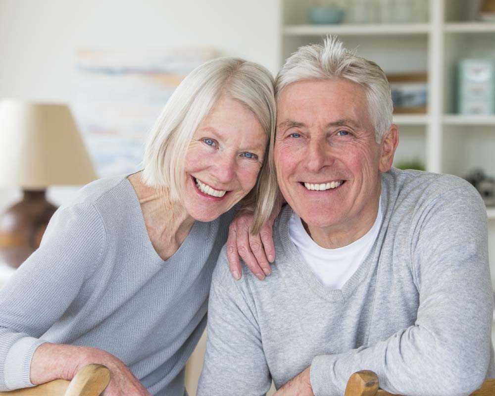 Senior couple in gray sweaters smiling showing off strong dental implants