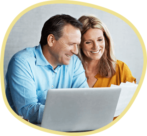 Man in a blue shirt and woman in a yellow shirt sitting in front of a computer smiling as they look through their financial options for dental implant cost.