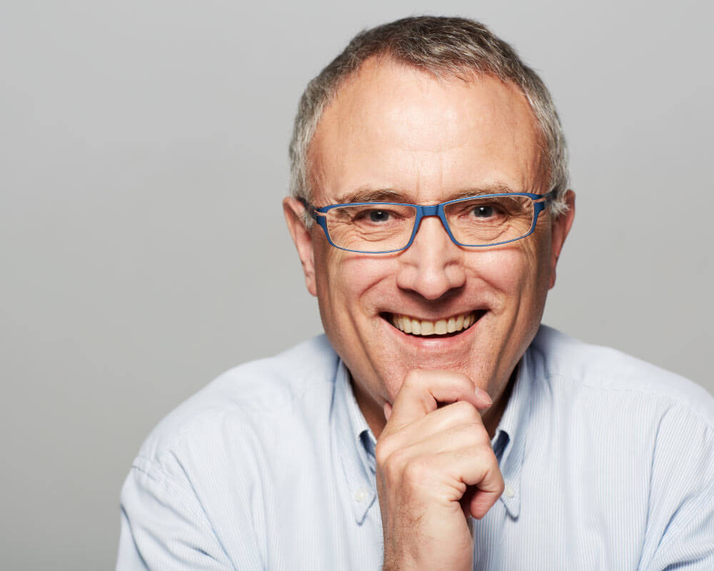 Senior man wearing glasses and smiling showing off dental implants