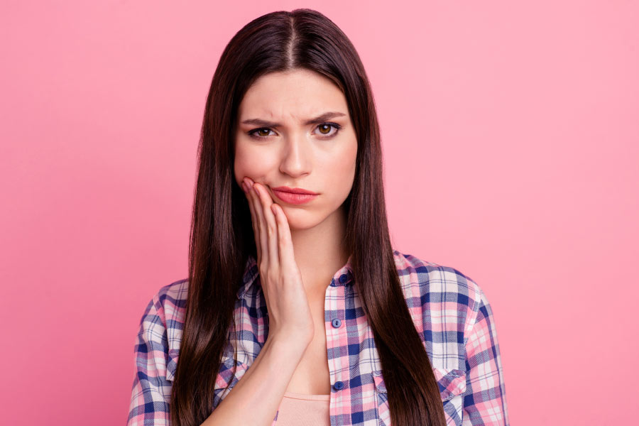 young woman holds her jaw and frowns because of tooth pain