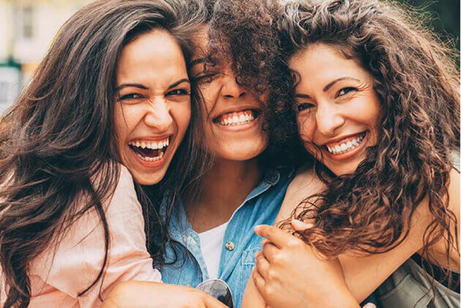 Three young women hug and smile