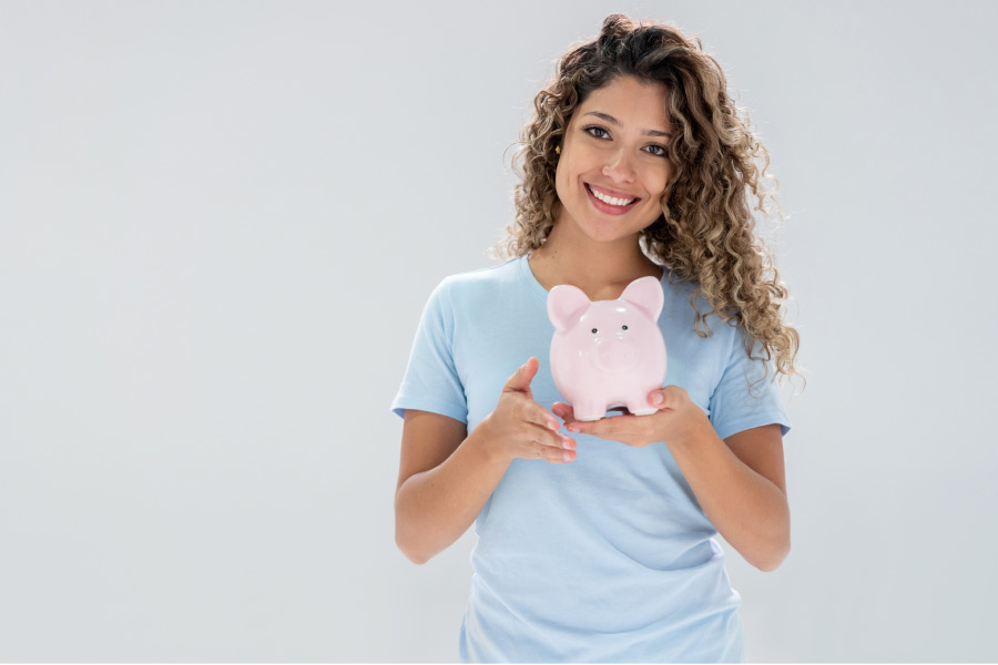 young woman holds a piggybank and smiles about affordable dentistry